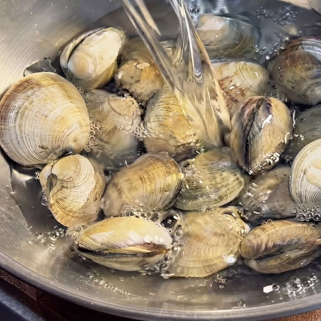 In einer Wasserschüssel eingetauchte Muscheln, die von Hand gründlich gereinigt werden.