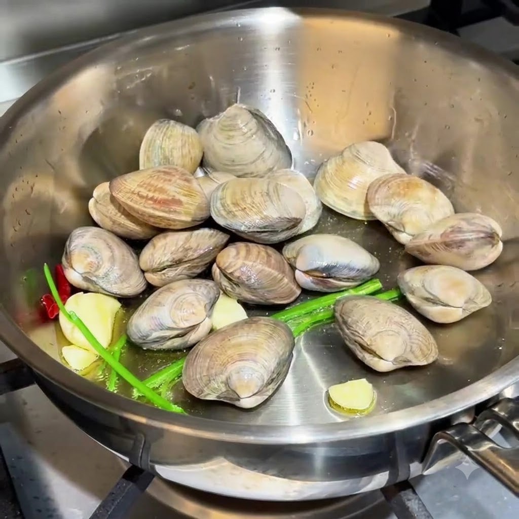 Muscheln, die neben Knoblauch und Schnittlauchwurzeln in der Pfanne verstreut sind.