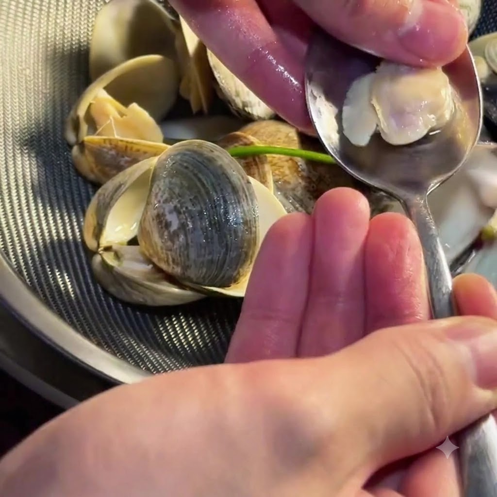 Eine Person benutzt einen kleinen Löffel, um zartes Muschelfleisch aus seiner Schale zu löffeln.