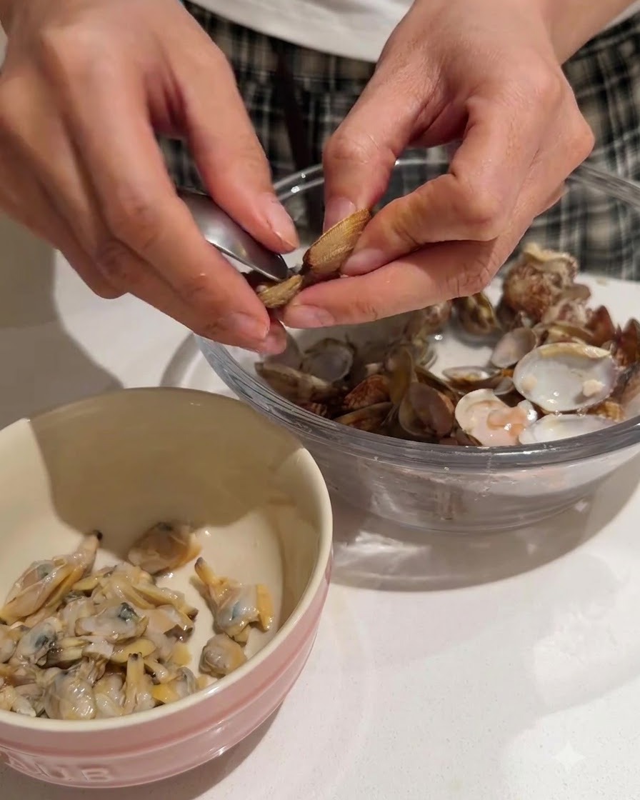 Hände lösen zartes Muschelfleisch aus den Schalen in eine Schüssel mit rosa Rand.