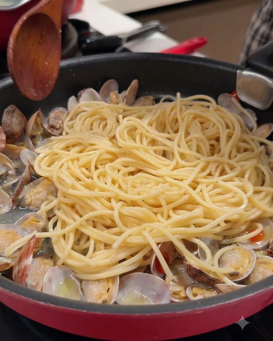 Ein Holzlöffel und Spaghetti in einer Pfanne mit geöffneten Muscheln und Brühe.