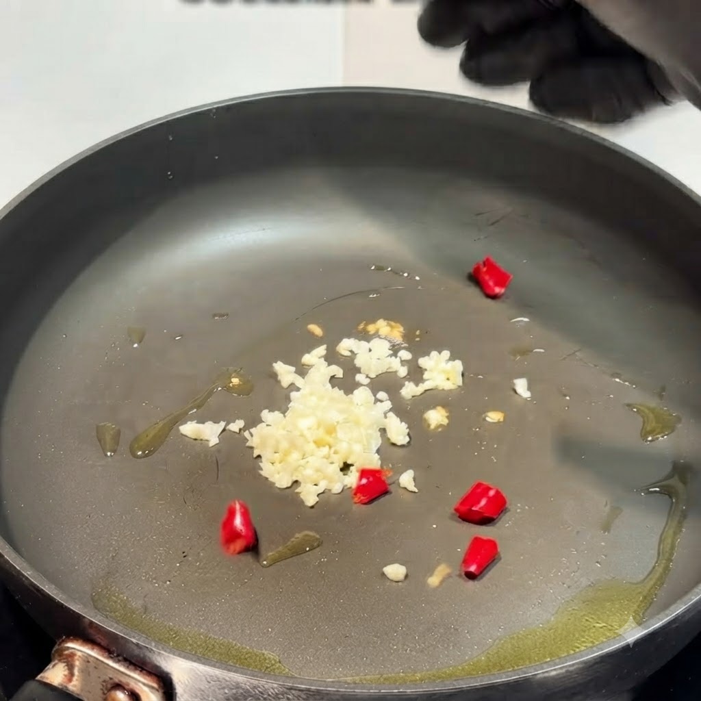 Gehackter Knoblauch und zerkleinerte rote Chilischoten sind in einer geölten Pfanne verteilt.