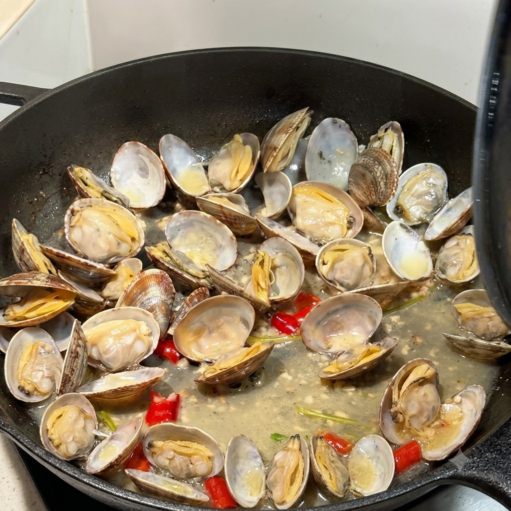 Geöffnete Muscheln garen in Brühe in einer Pfanne mit teilweise sichtbarem Deckel.