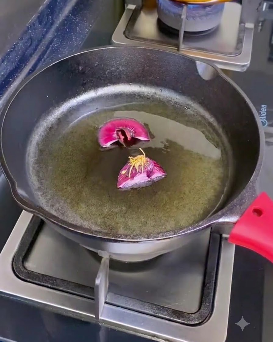 Eine Gusseisenpfanne auf einer Kochstelle mit Olivenöl und zwei geschnittenen Schalottenwurzeln.