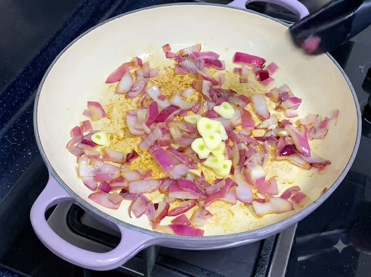 Frisch geschnittene Knoblauchstücke werden zu einer Pfanne mit angebratenen roten Zwiebeln gegeben.