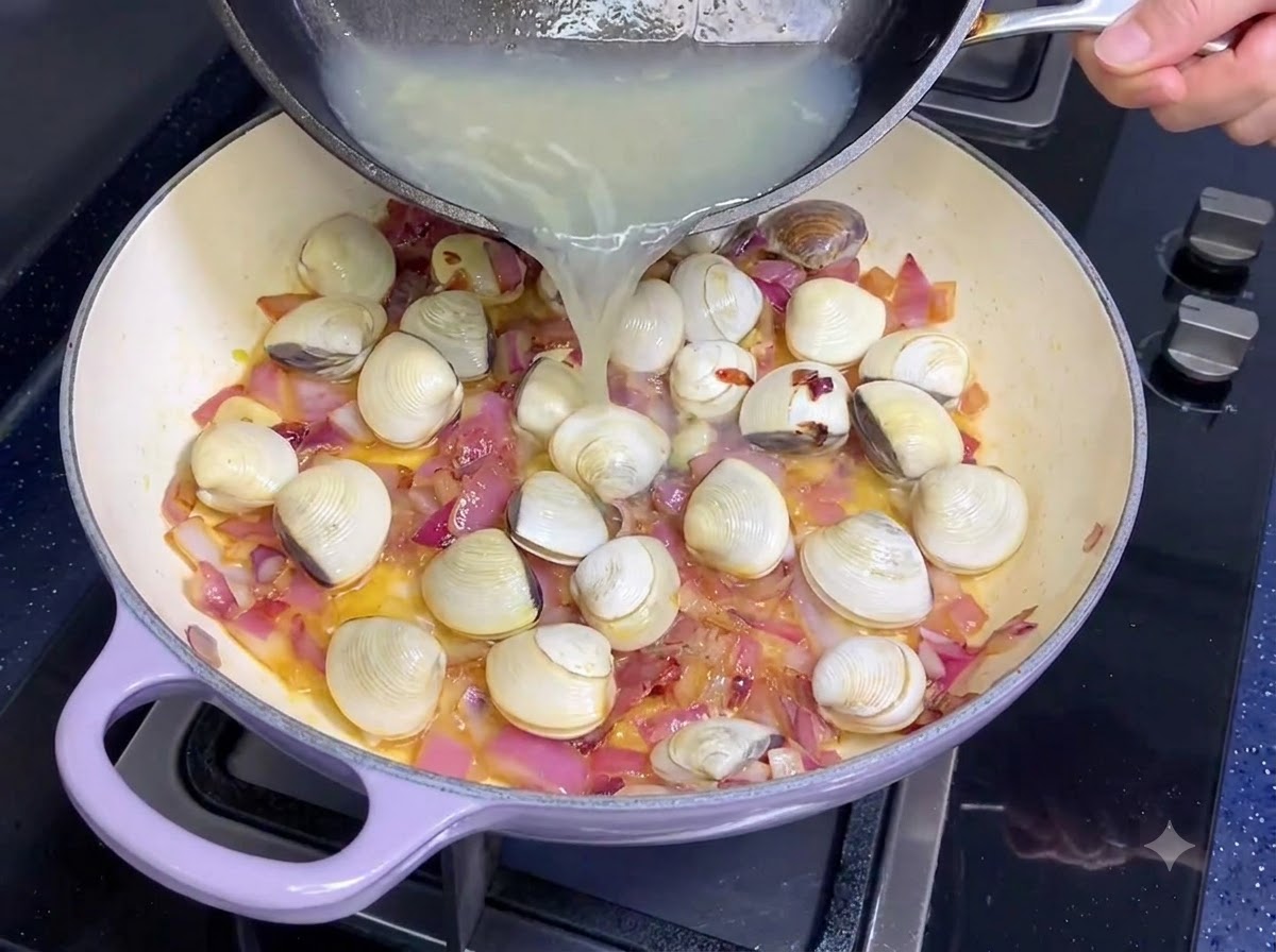 Muschelbrühe wird aus einer Pfanne in eine Pfanne mit Zwiebeln und Knoblauch gegossen.