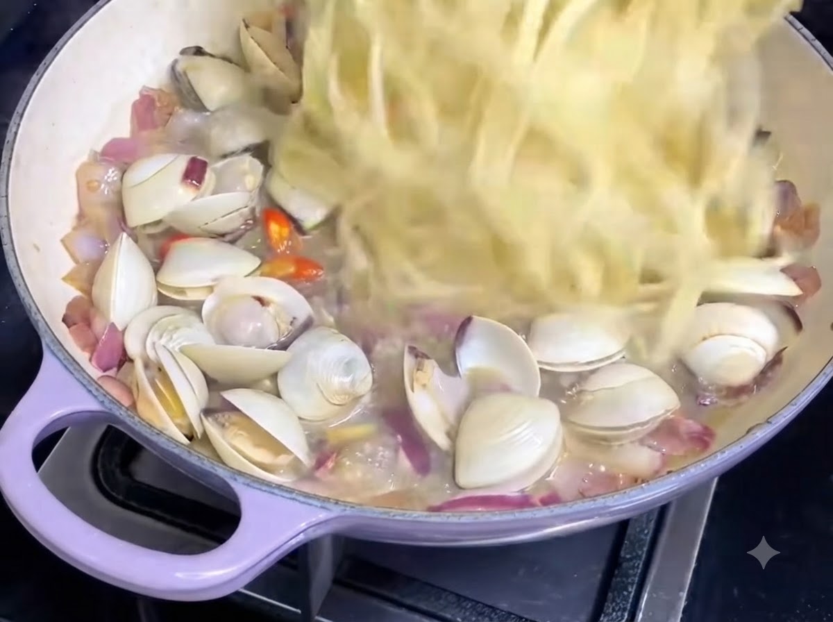 Gekochte Spaghettistränge werden in eine Pfanne mit Muschelsauce und Zwiebeln gegeben.