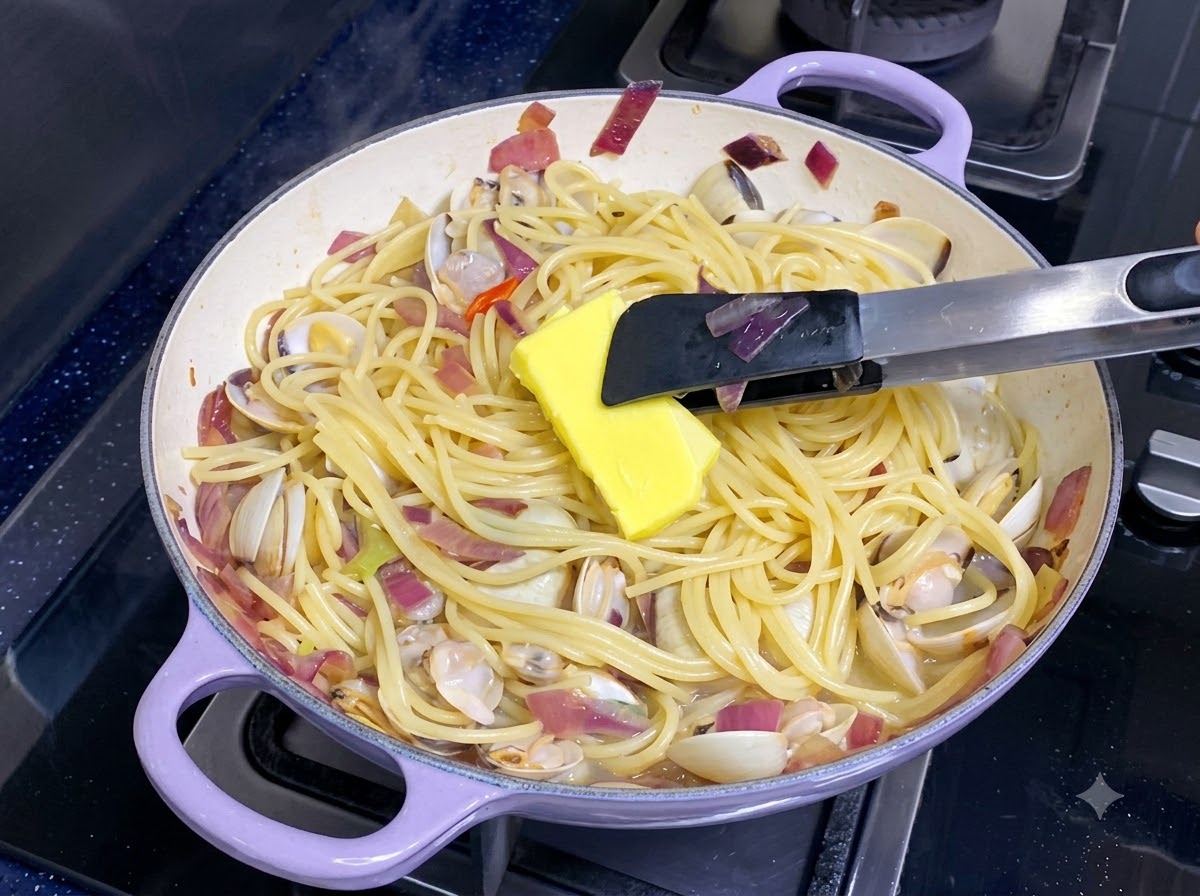 Ein Stück gelbe Butter schmilzt in einer Pfanne mit gemischten Spaghetti und Muscheln.