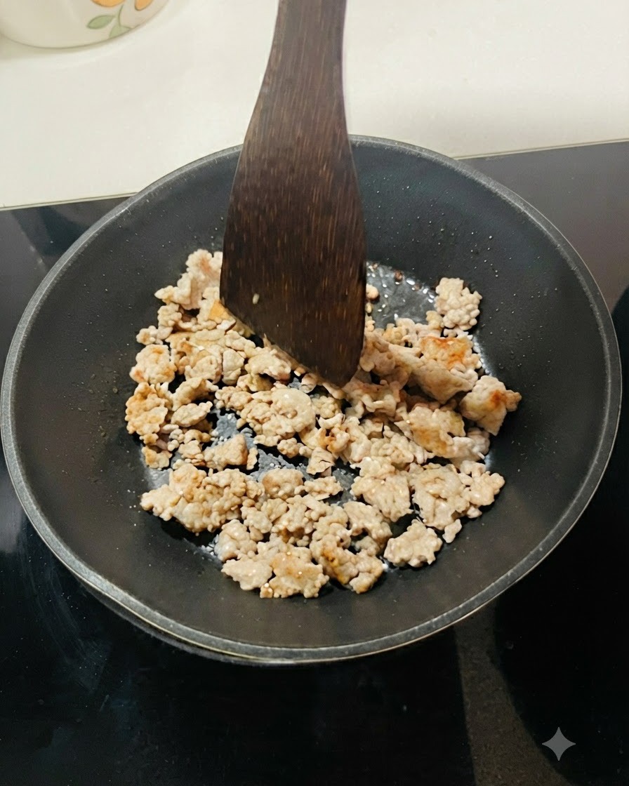 Hackfleisch wird in einer schwarzen Pfanne angebraten und mit einem Holzspatel in kleine Stücke geteilt.