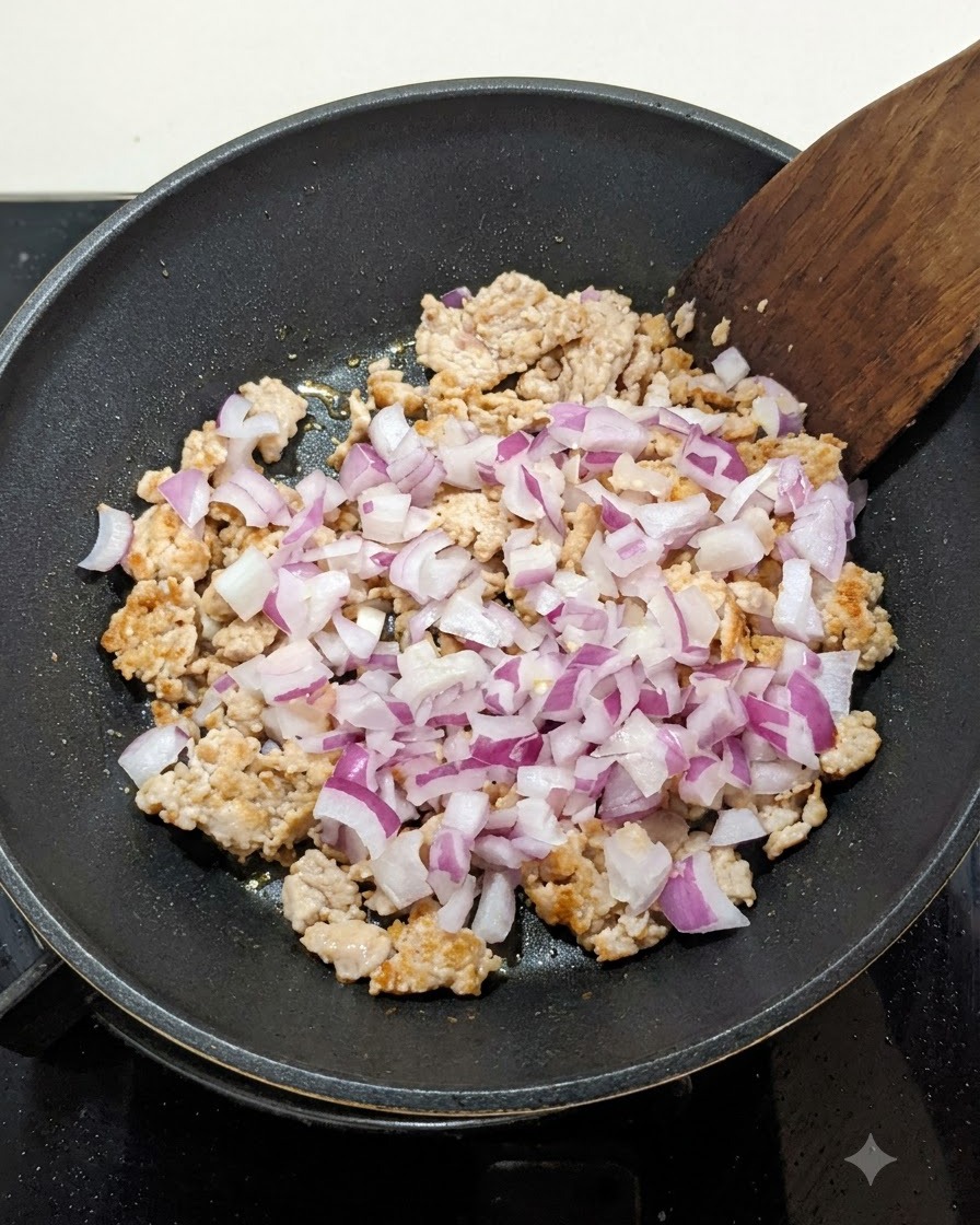 Gewürfelte rote Zwiebeln werden in einer Pfanne zum angebratenen Hackfleisch gegeben und mit einem Holzspatel verrührt.
