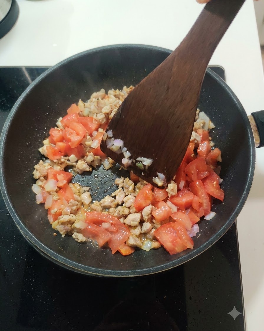 Frische gewürfelte Tomaten werden in einer Bratpfanne unter die Fleisch-Zwiebel-Mischung gerührt.