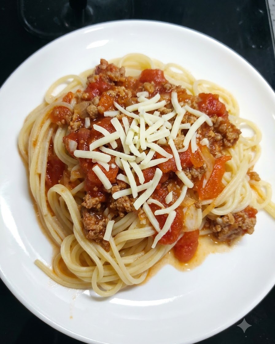 Geraspelter Mozzarella wird auf einem weißen Teller über Spaghetti mit Tomatensoße gestreut.