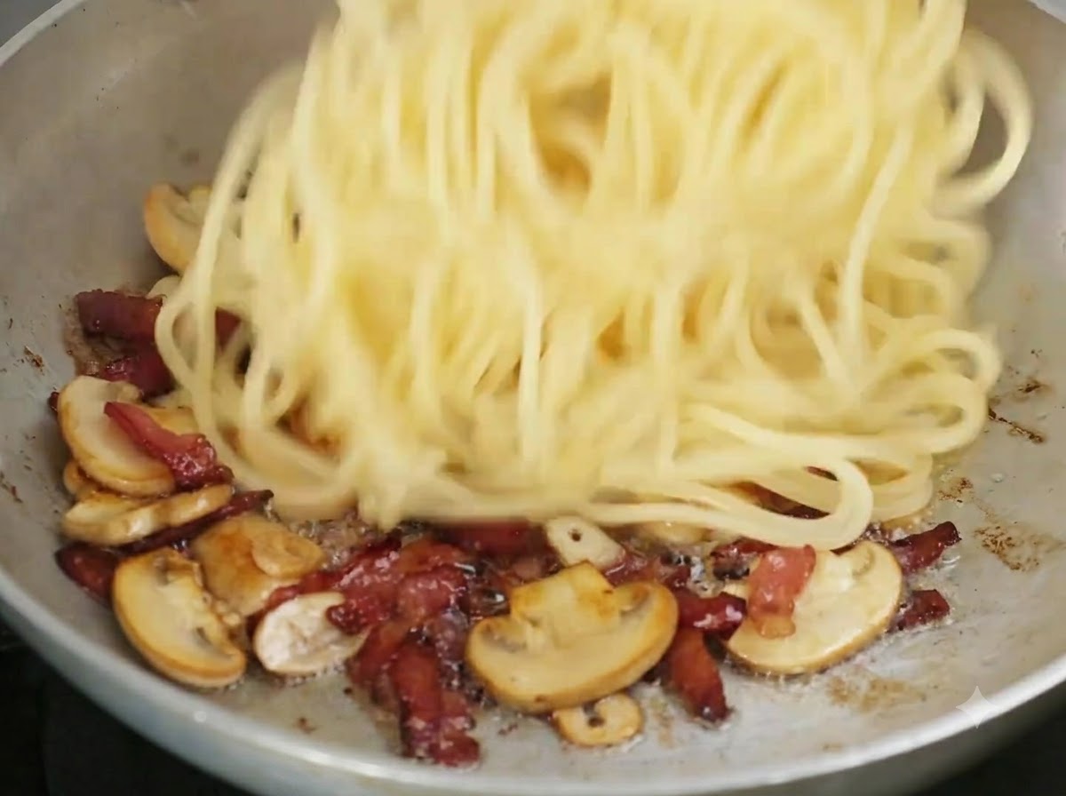 Gekochte Spaghetti werden in die Bratpfanne zu den gebratenen Zutaten gegeben.