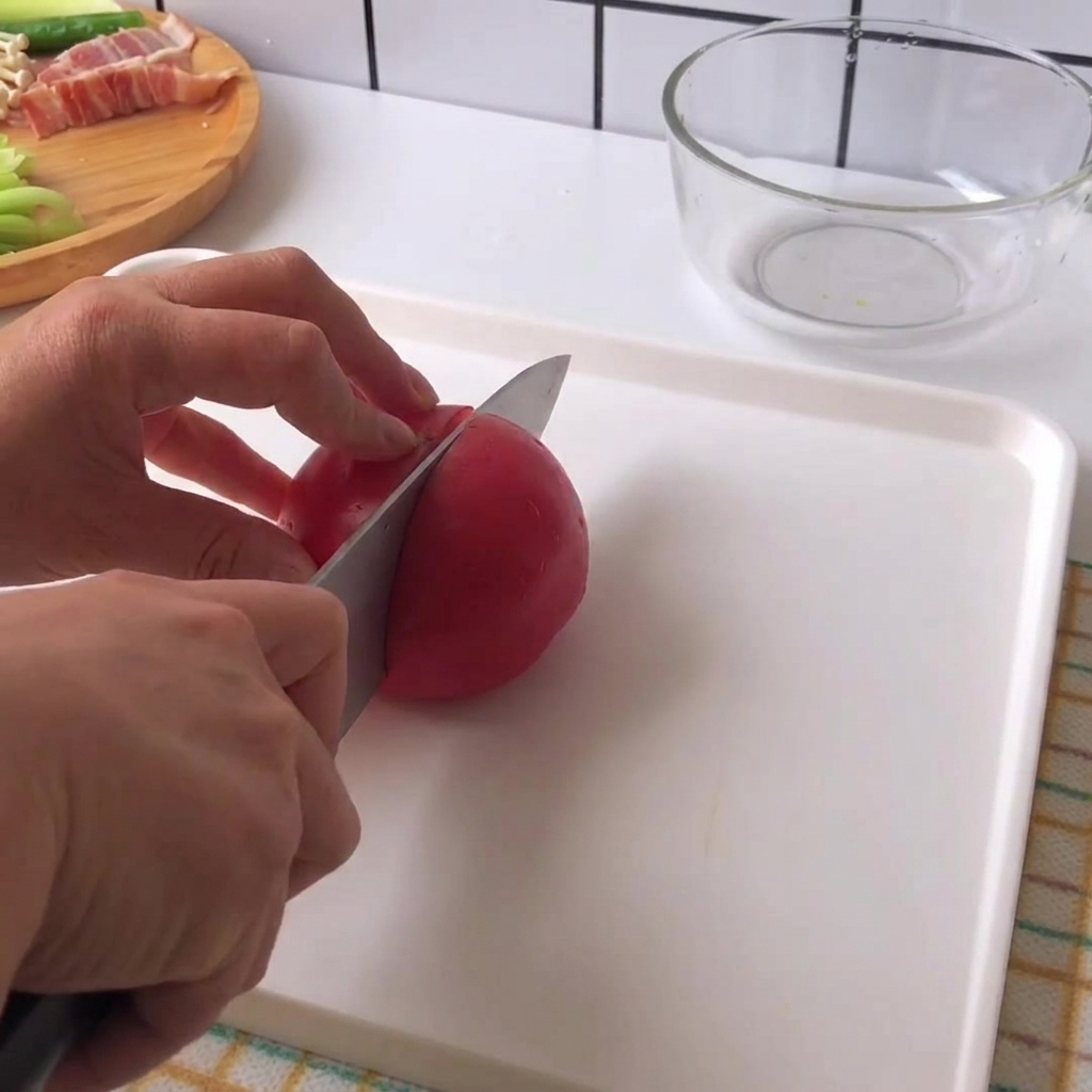Hände halten ein Messer und schneiden eine frische rote Tomate auf einem weißen Schneidebrett in Stücke.