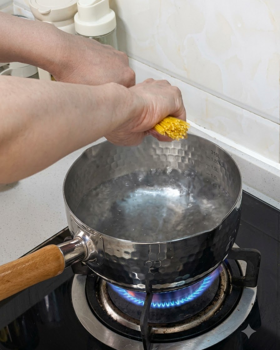 Ein Bündel Spaghetti wird in einen Topf mit kochendem Wasser auf einem Gasherd gegeben.