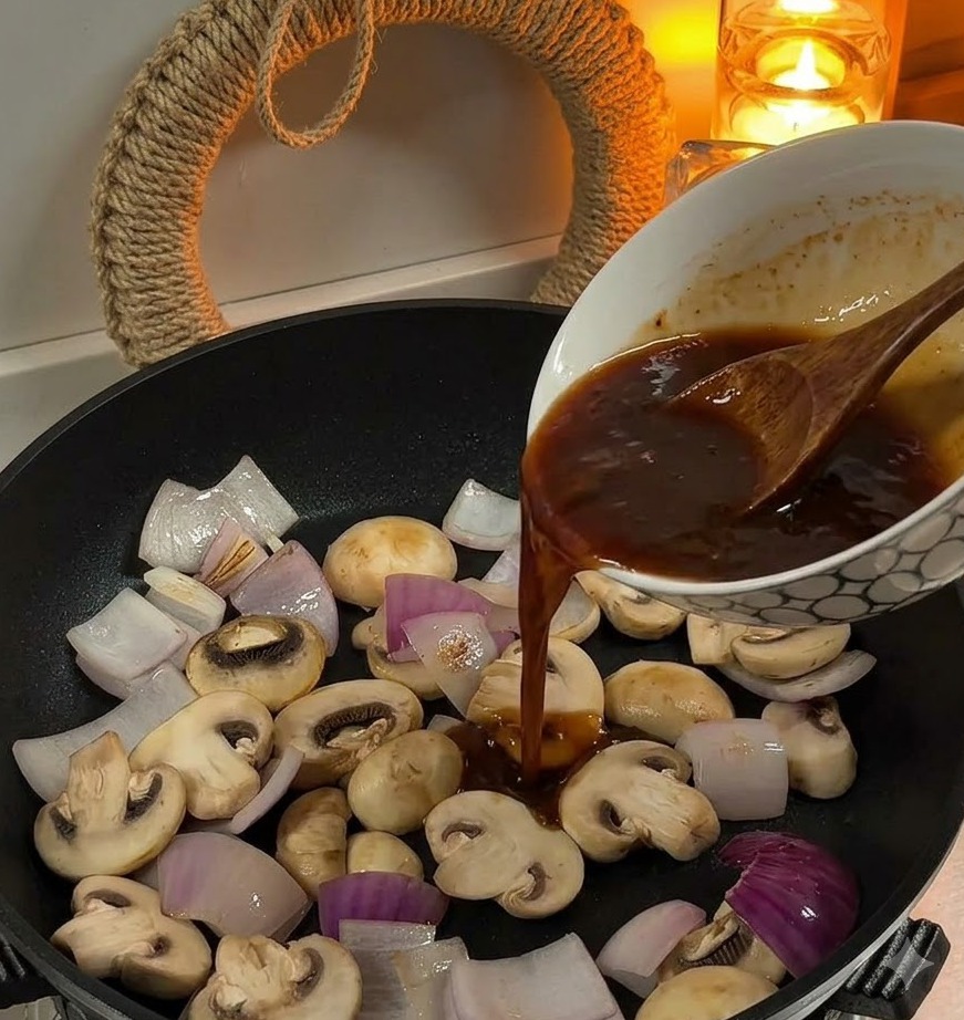 Braune Sauce wird aus einer Schüssel in eine Pfanne mit geschnittenen Zwiebeln und weißen Champignons gegossen.
