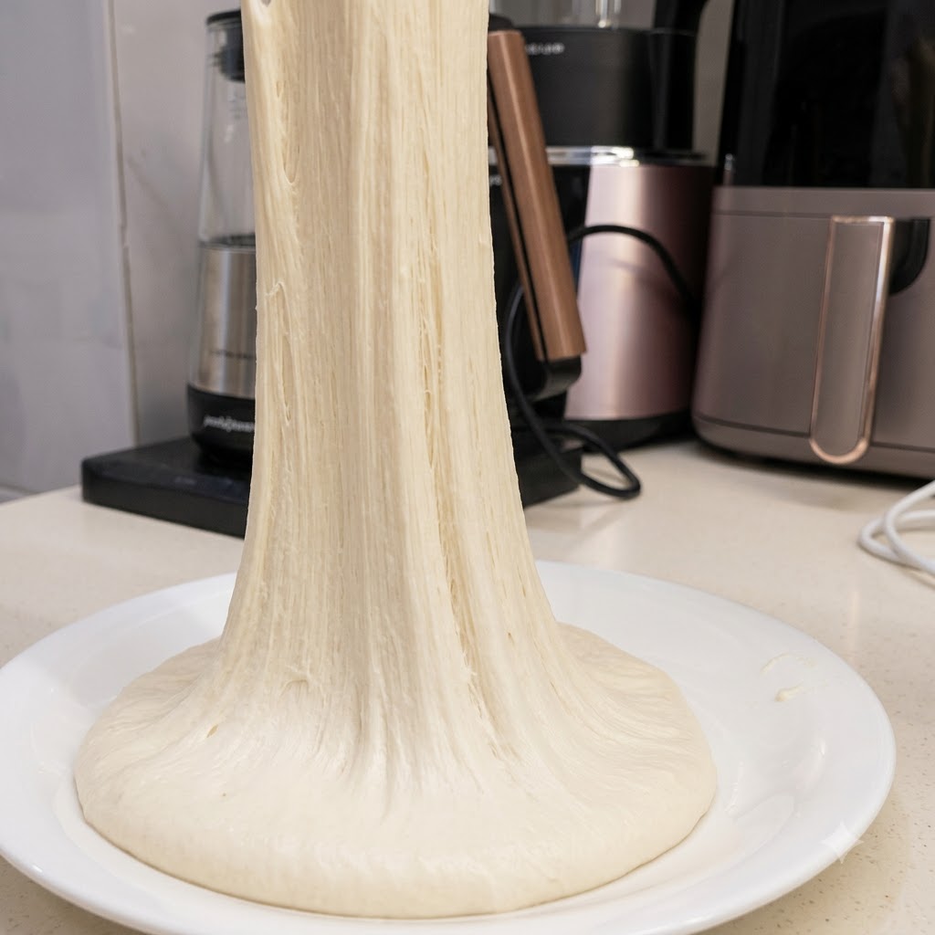 Ein langer Strang hochelastischen Pizzateigs wird nach oben gezogen.