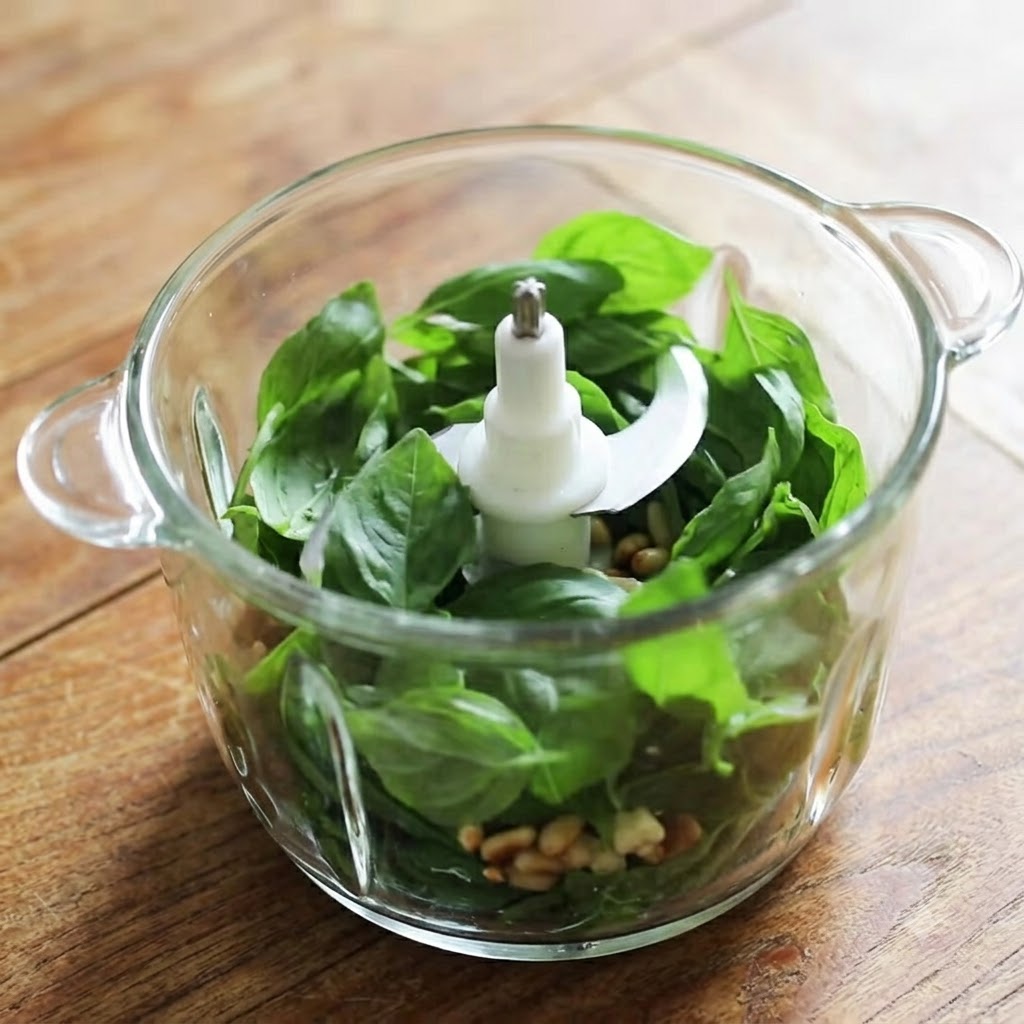 Ein Glasmixer, gefüllt mit frischen Basilikumblättern, Pinienkernen, Knoblauch und Käse, bereit zum Pürieren.