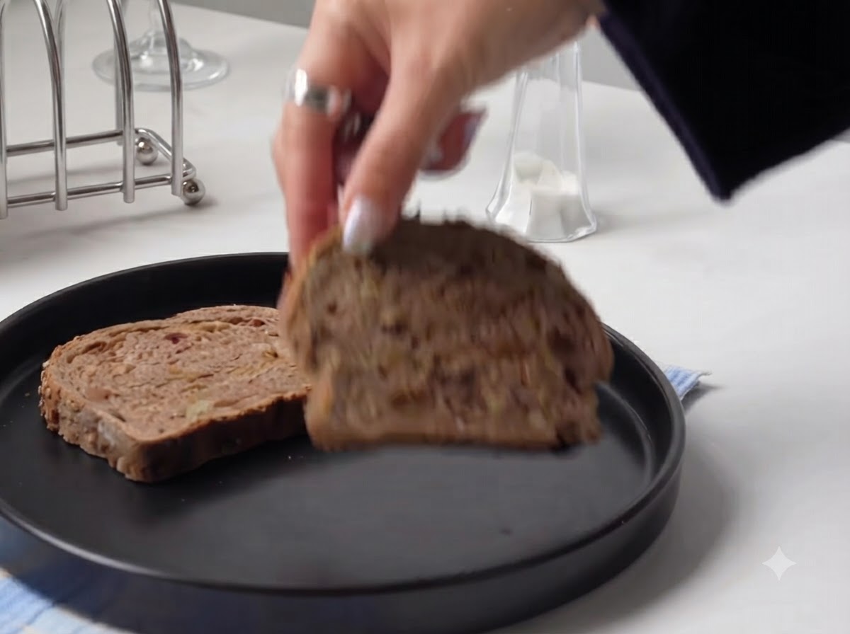 Eine Hand legt eine dicke Scheibe rustikales Brot auf einen runden schwarzen Teller.