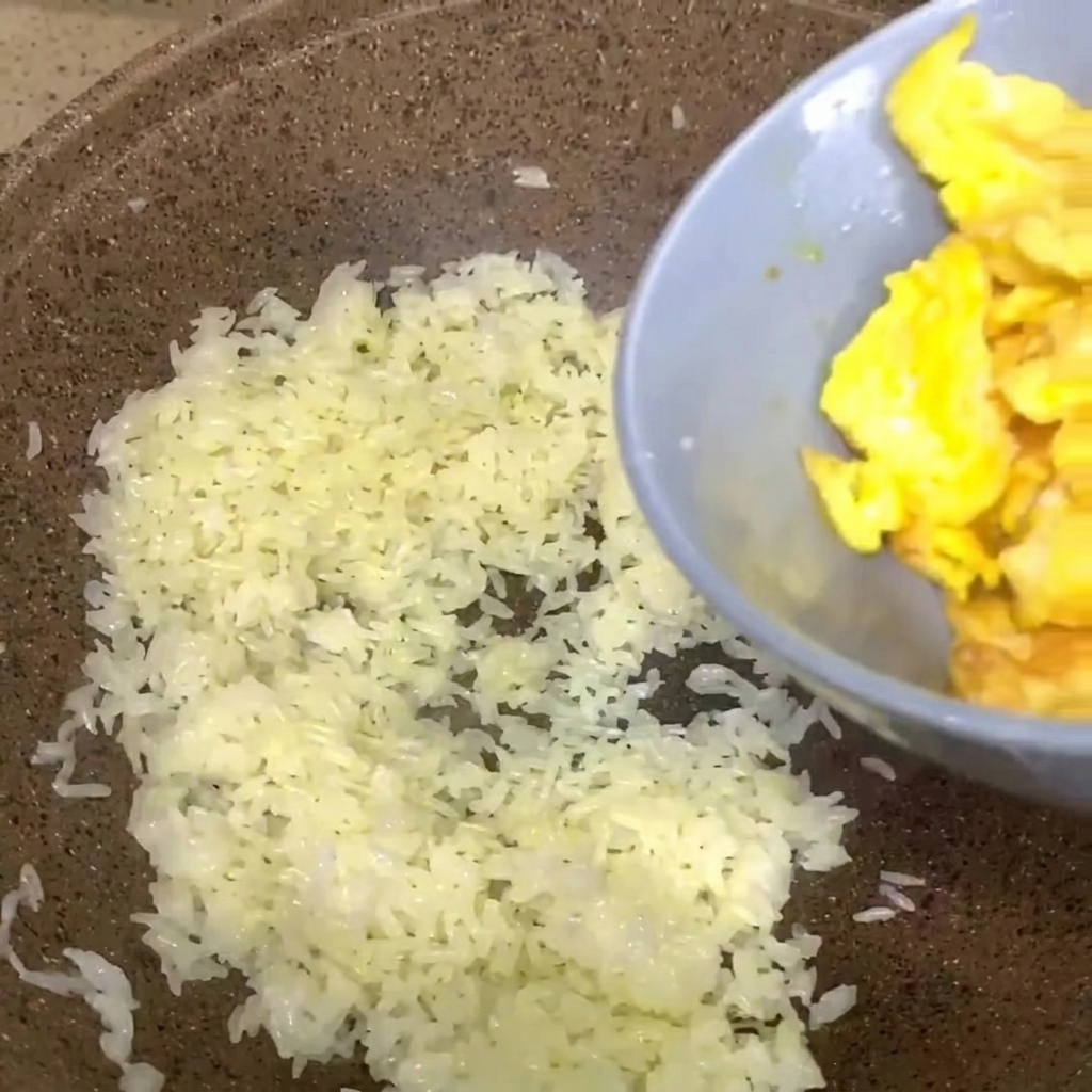Rührei aus einer grauen Schüssel wird in eine Pfanne mit weissem gekochten Reis gegeben.