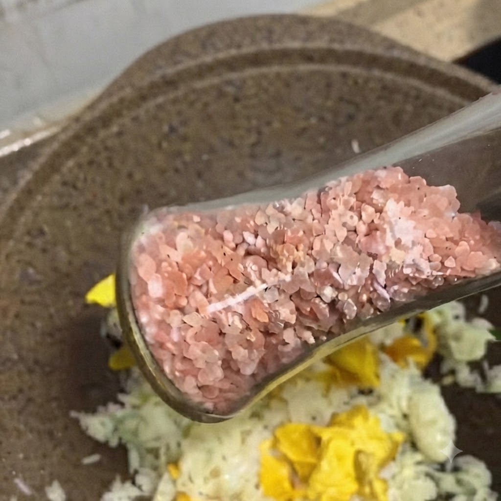 Eine Glasmühle streut Rosa Salzkristalle und schwarzen Pfeffer auf den Bratreis in einer Pfanne.