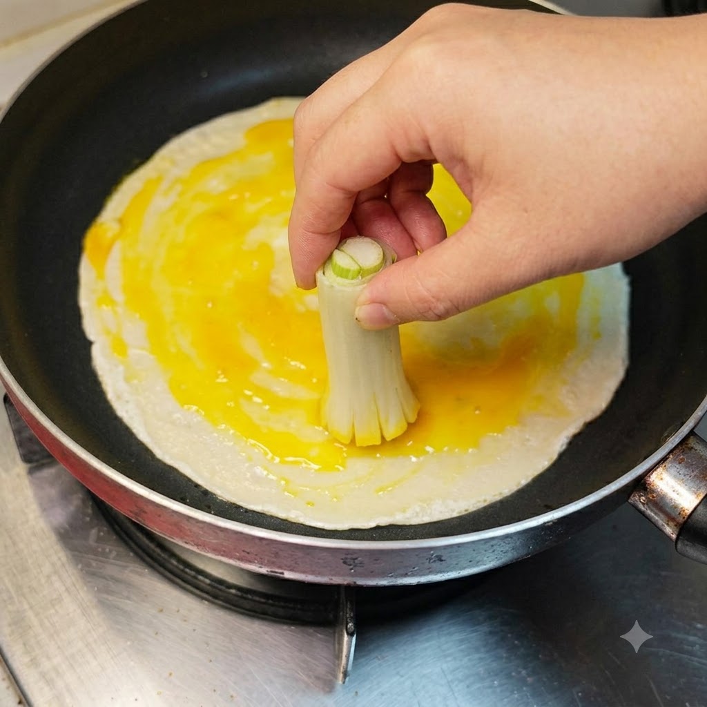 Eine Hand verstreicht mit gebündelten Frühlingszwiebelstangen Eiweiß und Eigelb auf einem Pfannkuchen.