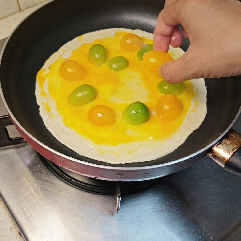 Gelbe und orangefarbene Kirschtomaten werden kreisförmig auf dem mit Ei bestrichenen Pfannkuchen angeordnet.