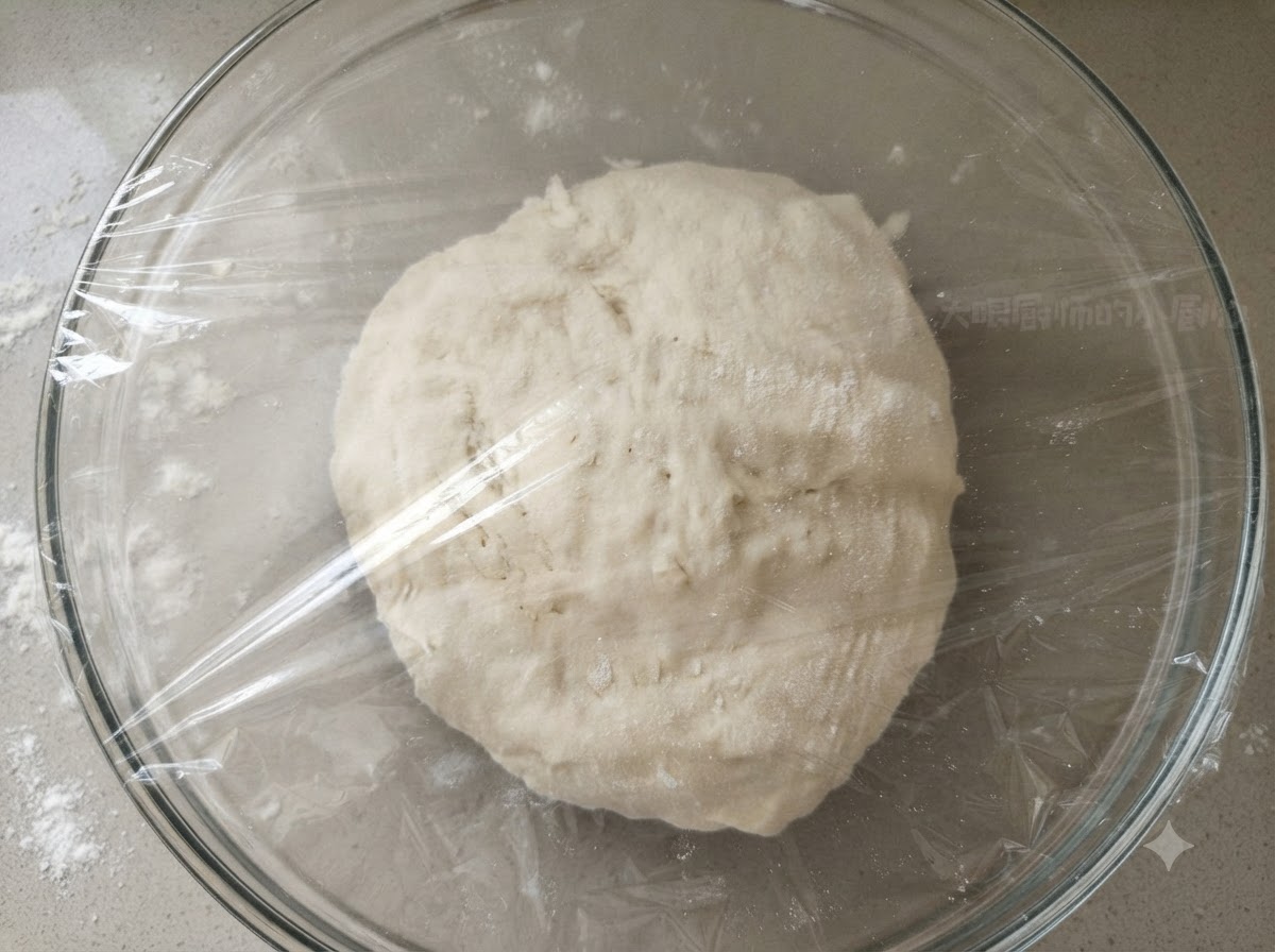 Eine glatte Teigkugel in einer klaren Glaschüssel, die fest mit Frischhaltefolie abgedeckt ist.