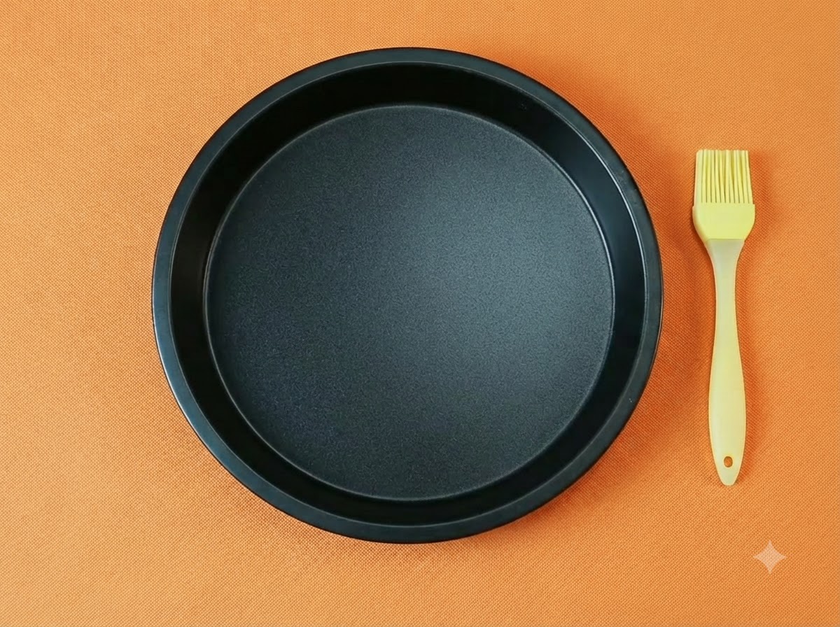 Eine leere, schwarze runde Pizzapfanne zusammen mit einem gelben Silikon-Ölpinsel vor orangefarbenem Hintergrund.