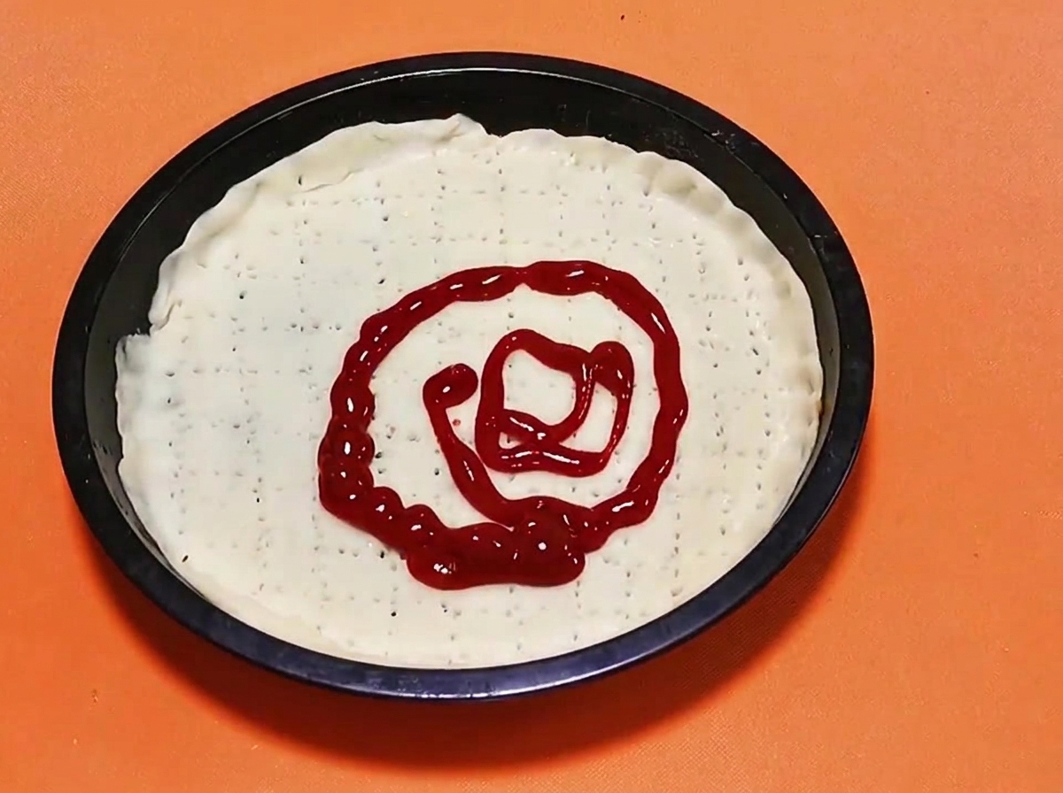 Ein spiralförmiges Muster aus hellroter Tomatensauce, die auf die Mitte eines rohen Pizzateigbodens gesprüht wird.