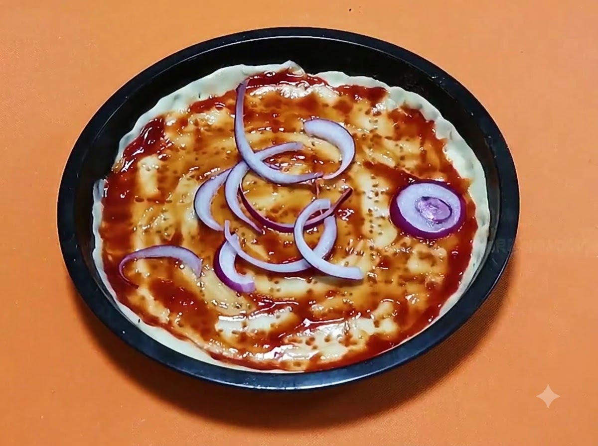 In Scheiben geschnittene rote Zwiebelringe auf einem mit Tomatensauce bestrichenen Pizzateigboden in einer schwarzen runden Backform.