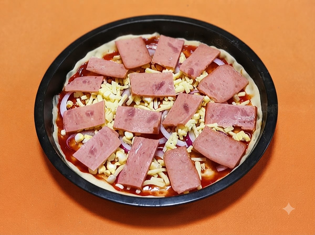 Rechteckige Scheiben rosa Schinkenscheiben systematisch auf einem mit Käse und Zwiebeln bedeckten Pizzateig ausgelegt.