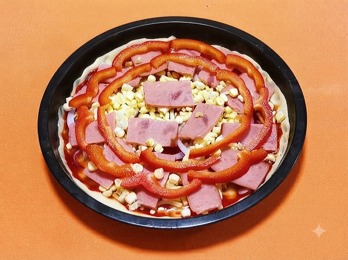 Pizzateig in einer schwarzen Pfanne, belegt mit Sauce, Schinken, gelben Maiskörnern und roten Paprikastreifen.
