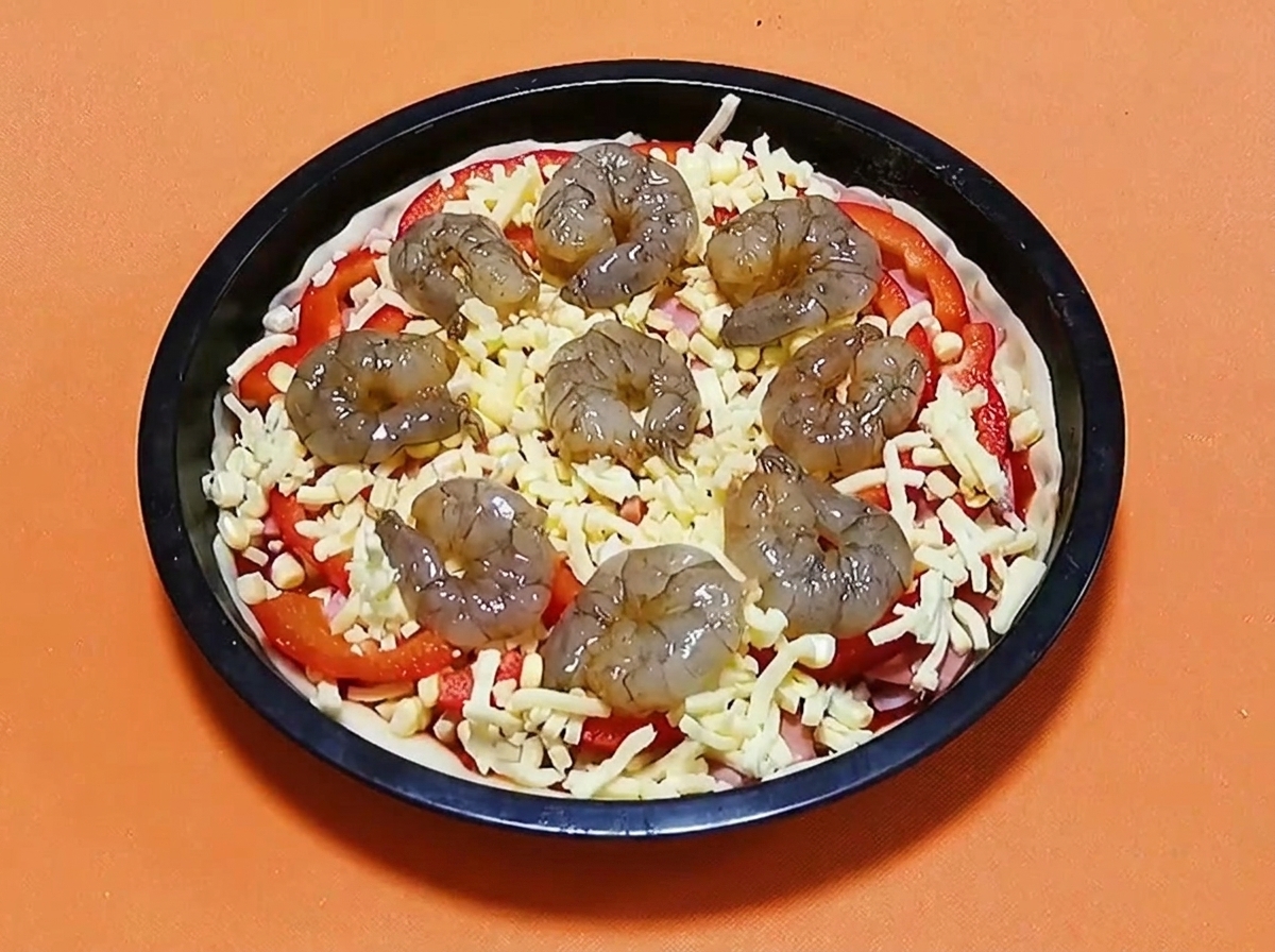 Rohe marinierte Garnelen in einem Kreis auf einer Pizza mit Käse, Paprika und Schinken angeordnet.