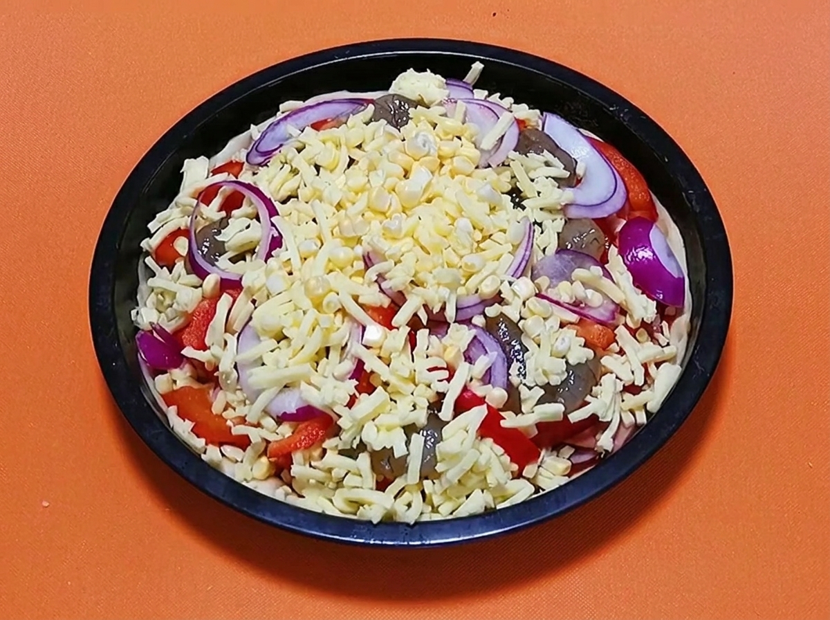 Vollständig belegte rohe Meeresfrüchte-Pizza, garniert mit einer finalen Schicht geriebenem Käse und roten Zwiebelringen, bereit zum Backen.