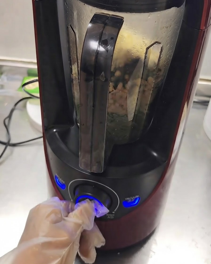 Ein Mixer in Betrieb, während sich die Zutaten im Inneren vermischen und eine Hand den Regler dreht.
