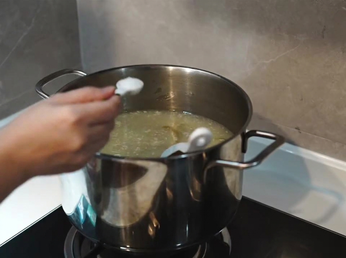 Ein Löffel Salz wird in einem Edelstahltopf zu einer köchelnden, eingedickten, milchig-weißen Basisbrühe gegeben.