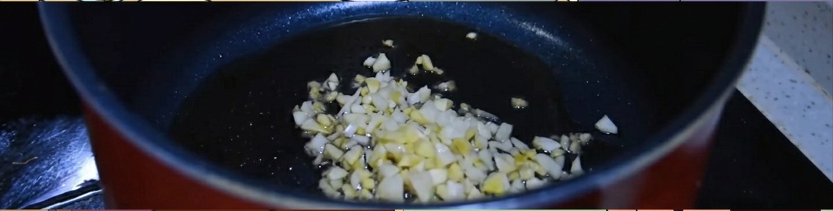 Gehackter Ingwer und Knoblauch brutzeln in einem dunklen Topf mit heißem Sesamöl.