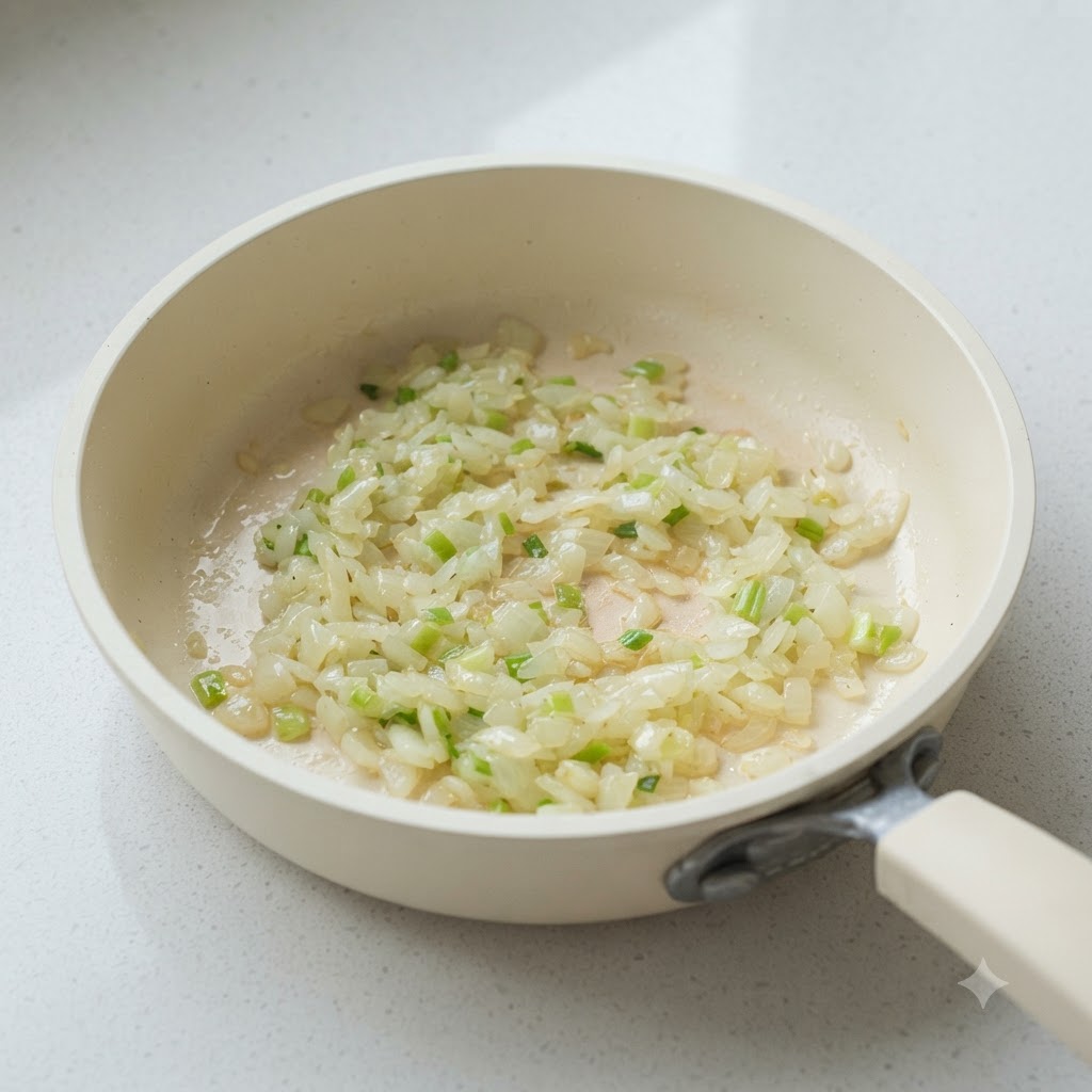 Gehackte Zwiebeln und weiße Lauchzwiebelteile in einer weißen Pfanne beim Anbraten.