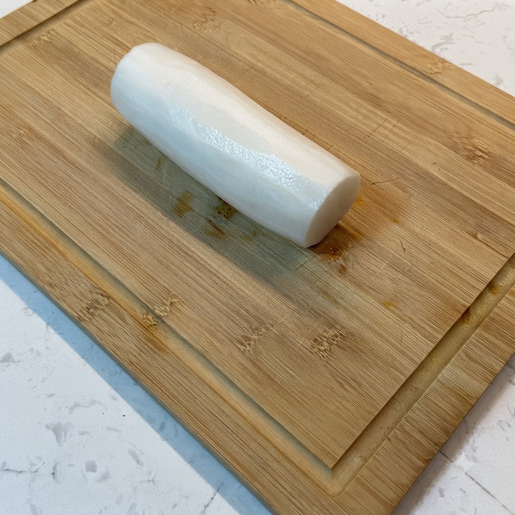 Ein weißer Rettich wird auf einem Holzschneidebrett in feine Streifen geschnitten.