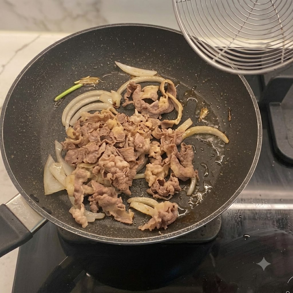 Blanchierte Rinderstreifen vermischt mit Zwiebeln in einer Bratpfanne.