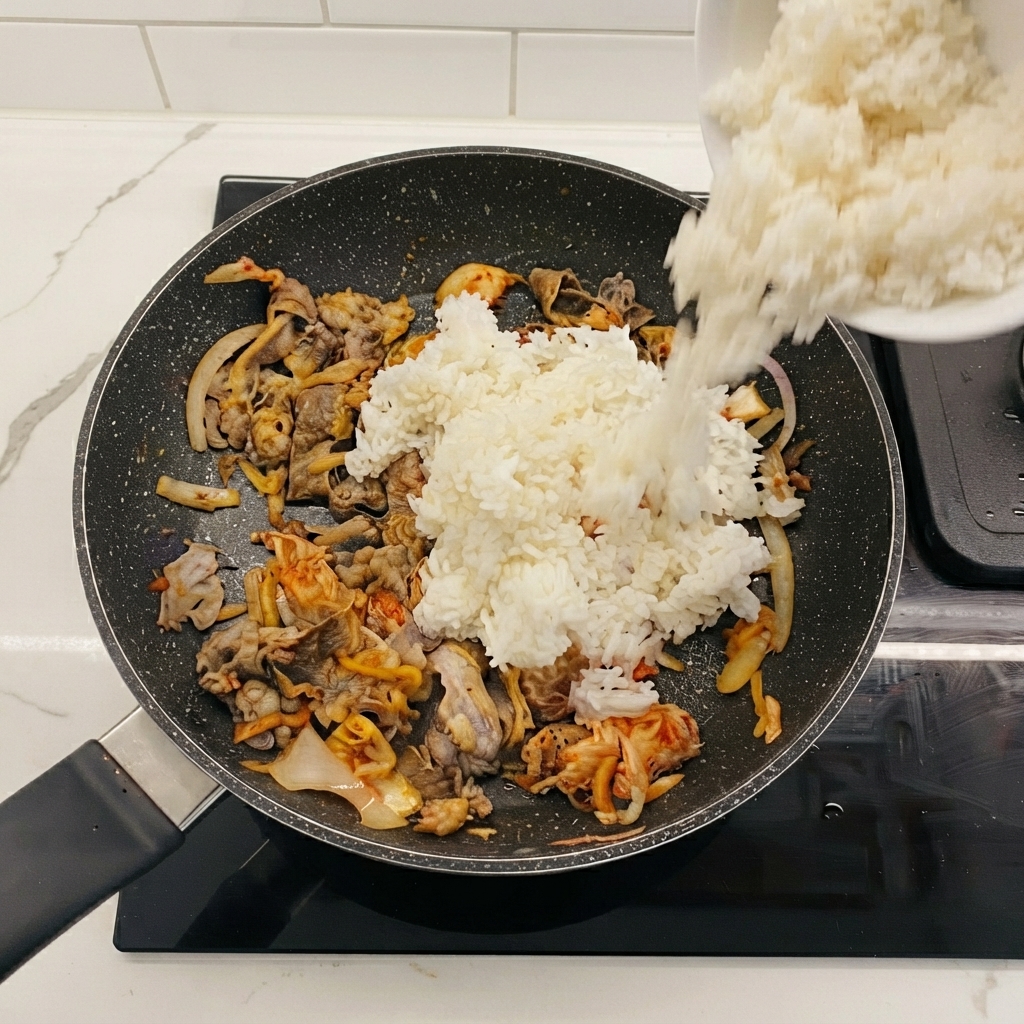 Weißer Reis wird aus einer Schüssel in die Bratpfanne mit Rindfleisch und Kimchi geschüttet.