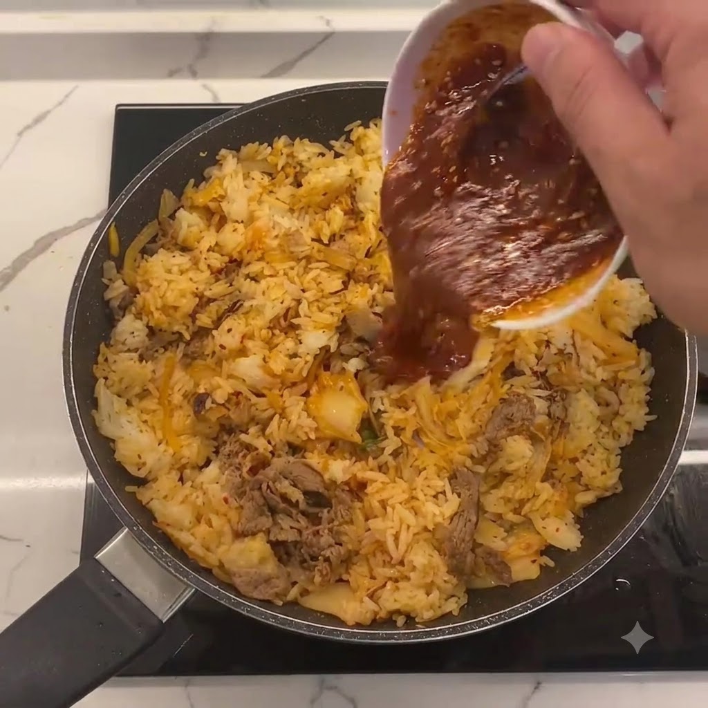 Spezialsauce wird aus einer kleinen weißen Schüssel in die Mitte der Pfanne mit Bratreis, Kimchi und Rindfleisch gegossen.