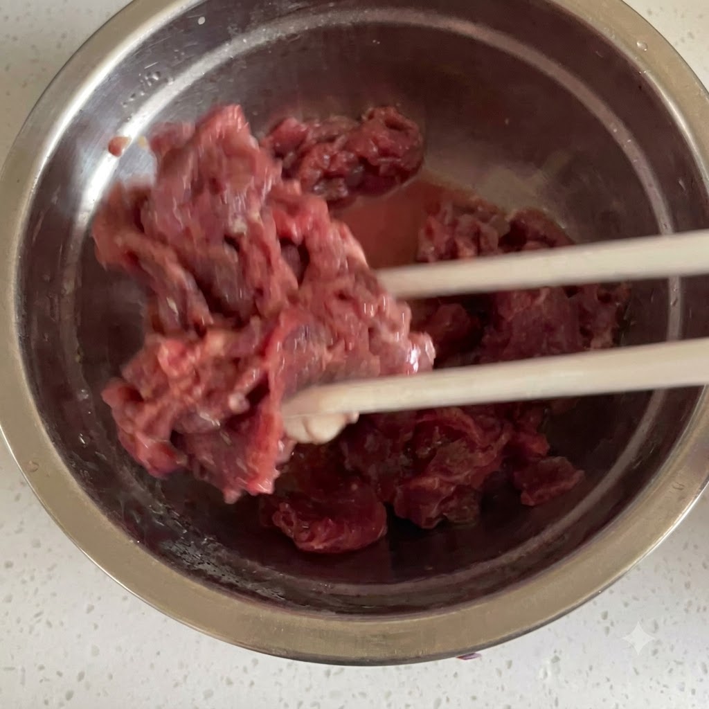 In dünne Streifen geschnittenes rohes Rindfleisch wird in einer Edelstahlschüssel mit den Marinadenzutaten vermischt.