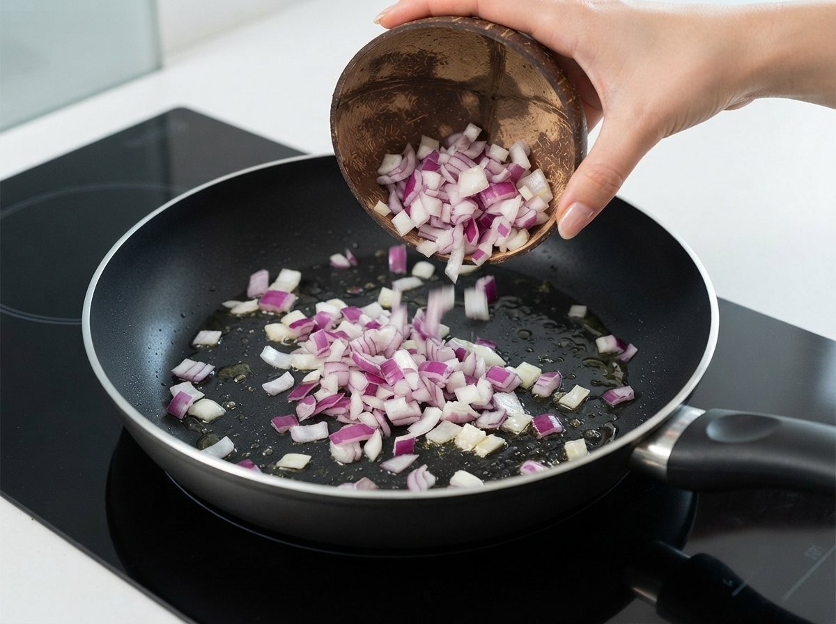 Gewürfelte rote Zwiebeln werden aus einer Kokosschale in eine Bratpfanne mit Öl gegeben.