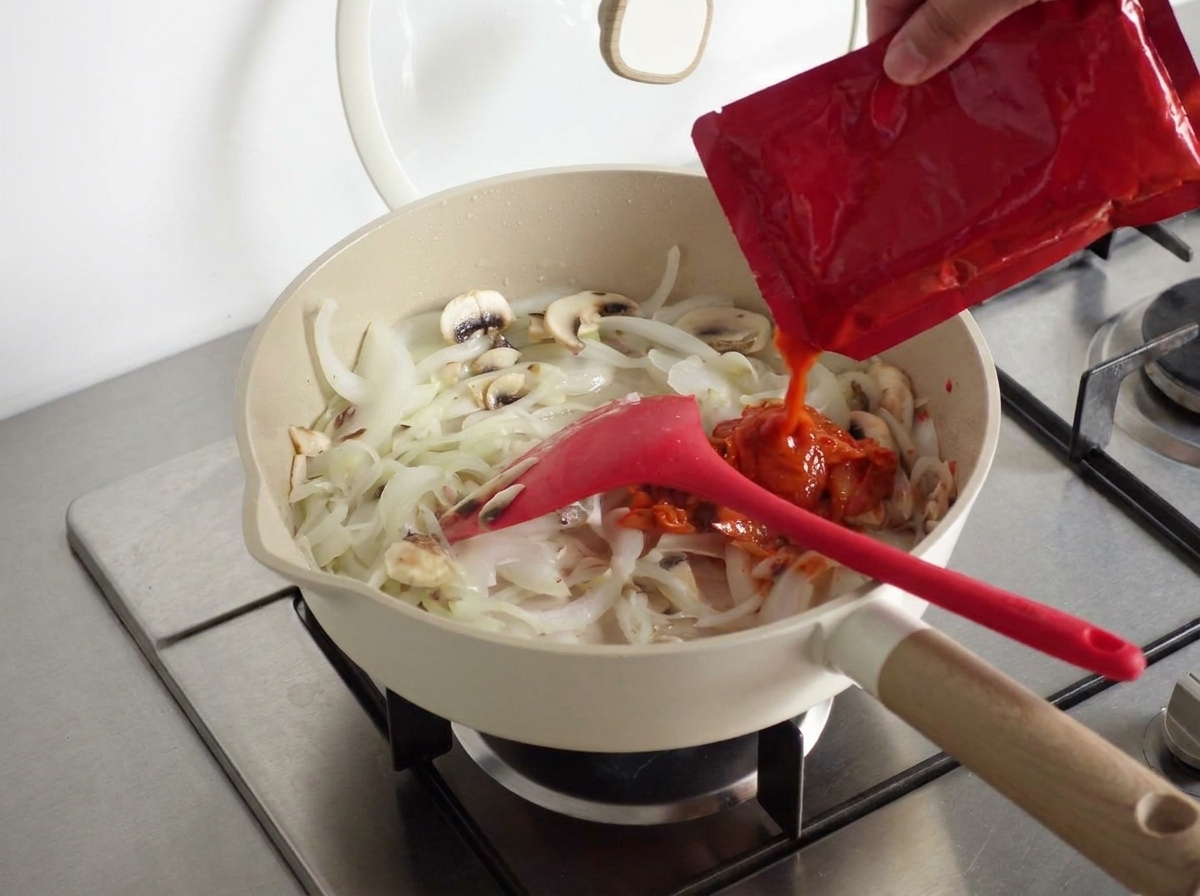 Ein Löffel koreanische scharfe Paste wird zu der Mischung in der Pfanne gegeben.
