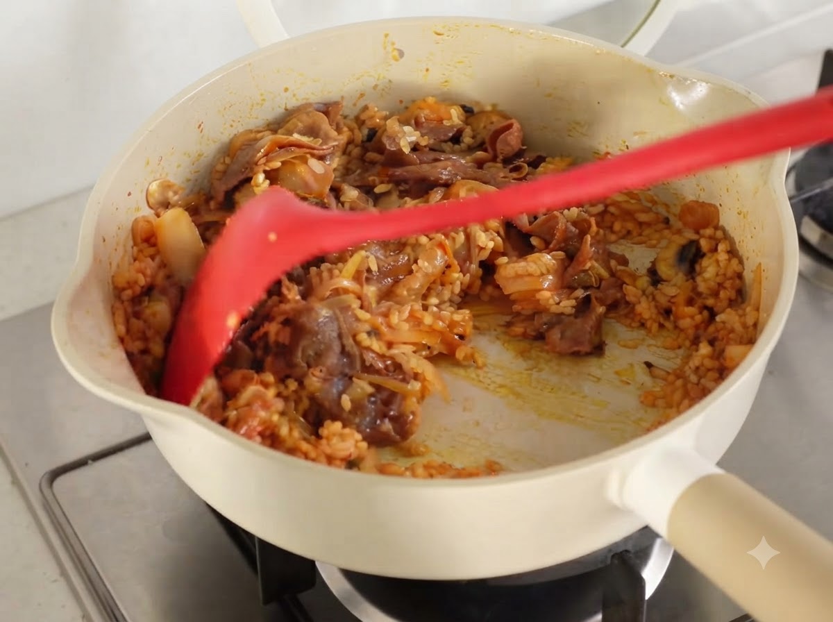 Alle Zutaten und der Reis werden in einer Pfanne gründlich zusammen angebraten, bis sie mit Kimchi-Saft überzogen sind.