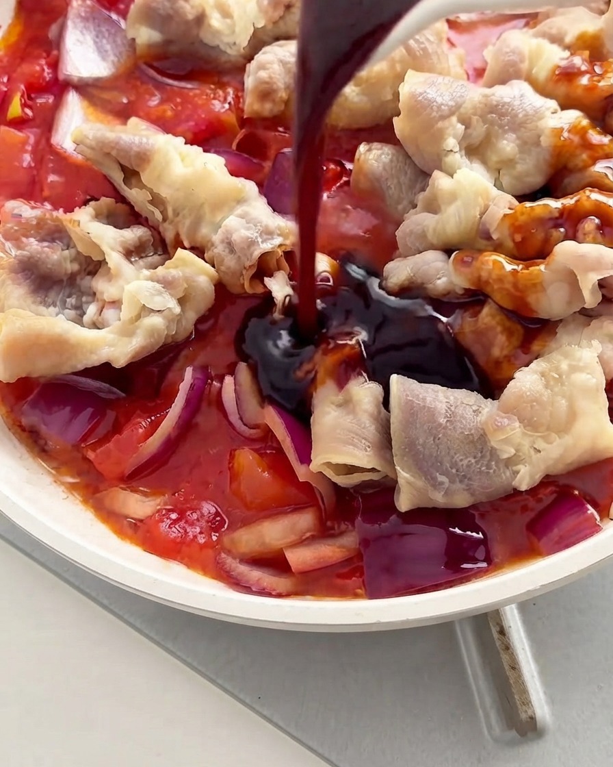 Dunkle Soße wird von einem Löffel auf die Rindfleischröllchen und Tomaten in einer weißen Pfanne gegossen.