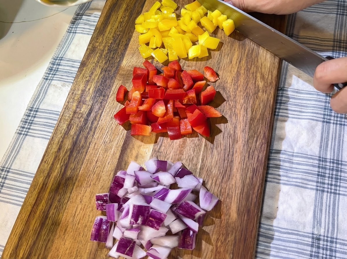Haufen von frisch gehackter roter und gelber Paprika sowie gewürfelten roten Zwiebeln, ordentlich auf einem Holzschneidebrett angeordnet.