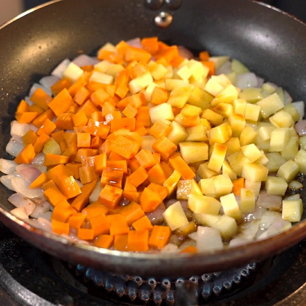 Dunkle Sojasauce wird in einer Pfanne über gewürfelte Karotten und Kartoffeln gegossen.